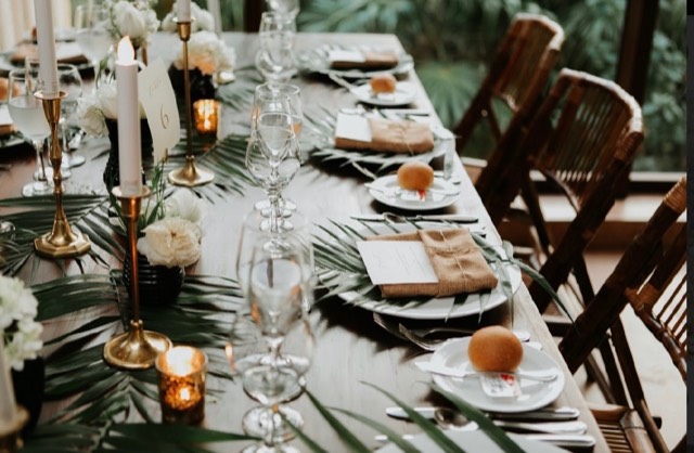 Coastal Celebrations tablescape detail — brass candlesticks, tropical palm leaf runner, and ivory florals on a dark wood table — Lux Events by Michelle